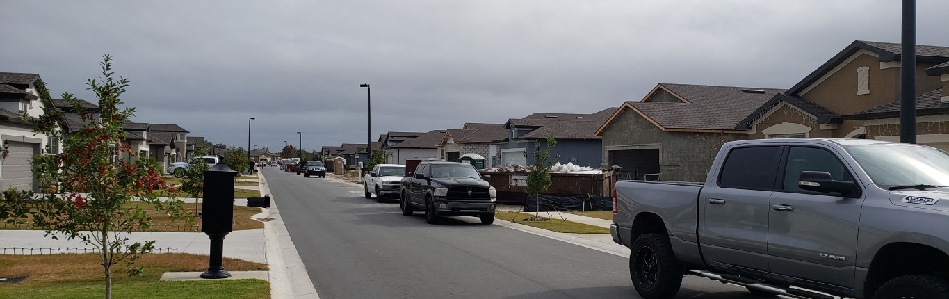 a street of new homes lined with trucks and a dumpster
